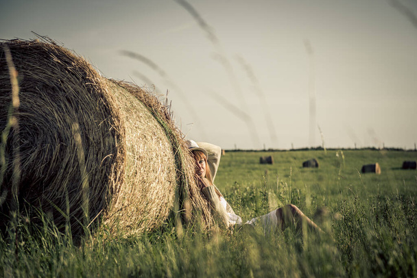 Hermosa chica está descansando después del trabajo. chica en el campo con heno. Mujer cerca de una gavilla de heno en un campo. La vida rural. Vacaciones en el pueblo
 - Foto, Imagen