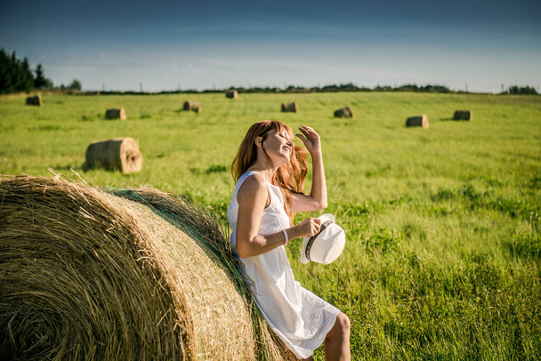 Kaunis tyttö lepää töiden jälkeen. Tyttö pellolla heinän kanssa. Nainen heinänvarren lähellä pellolla. Maaseudun elämää. Lomat kylässä - Valokuva, kuva