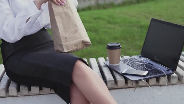 Felismerhetetlen üzletasszony croissant-t eszik és kávét iszik a parkban - Felvétel, videó