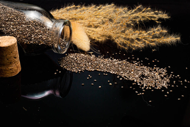 close-up view of dry chia seeds and glass jar on black background - Fotografie, Obrázek