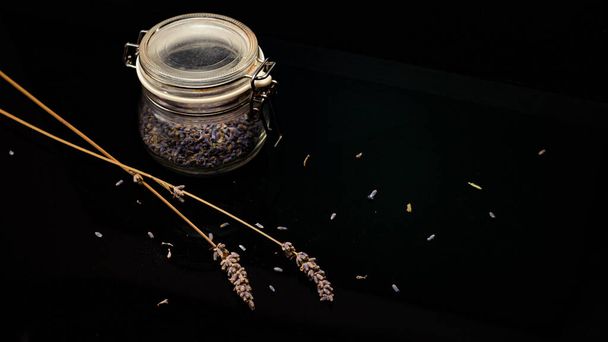 close-up view of lavender seeds and glass jar on black background, high angle view - Photo, Image