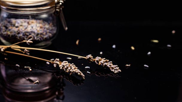 close-up view of lavender seeds and glass jar on black background - Fotografie, Obrázek