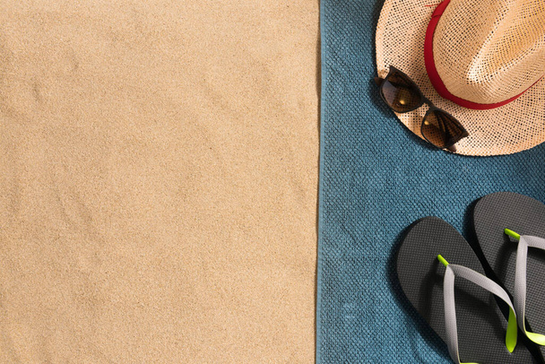 Summer vacation composition. Flip flops, hat and sunglasses on sand background. Travel vacation concept. Summer background. Border composition made of towel - Photo, image