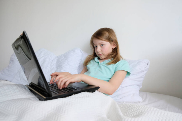 little girl sitting at a laptop and doing homework. baby with laptop in bed - Valokuva, kuva