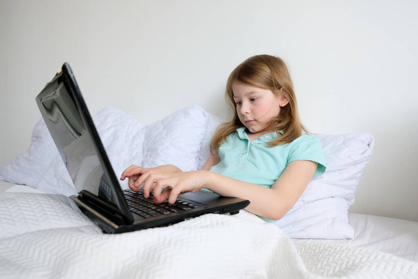menina sentada em um laptop e fazendo lição de casa. bebê com laptop na cama
 - Foto, Imagem