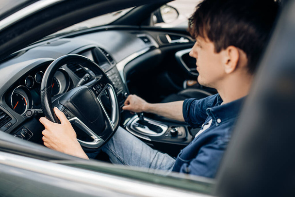 Sürücü koltuğunda oturan genç bir adam bir araba galerisinde arabayı test ediyor.. - Fotoğraf, Görsel