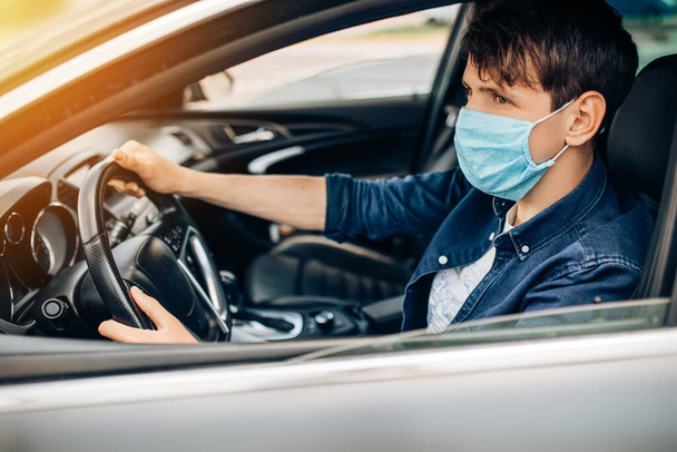 A young Man driving a car in a medical mask during an epidemic, a taxi driver in a mask, protection from the virus. Quarantine, coronavirus - Photo, Image