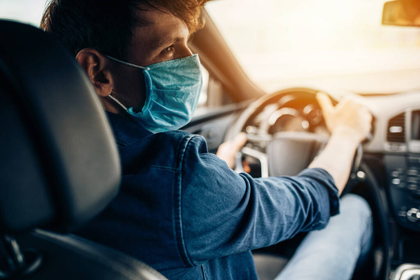 A young man in a protective medical mask, sitting at the wheel of a car, the driver is driving. Quarantine, coronavirus - Fotoğraf, Görsel