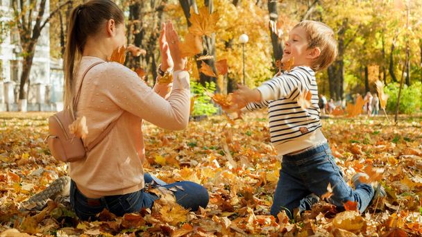 Little boy throwing fallen autumn leaves at his mother at park - Photo, Image