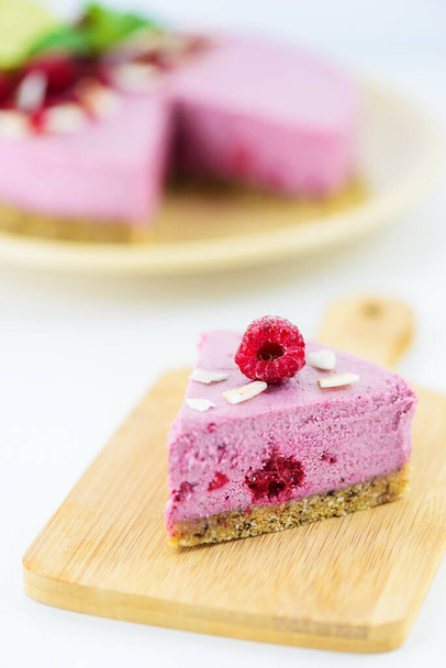 Slice of homemade raw cashew cake with raspberries, mint and lime on a light table. Vegan dessert, sugar free, gluten free, lactose free. - Фото, зображення