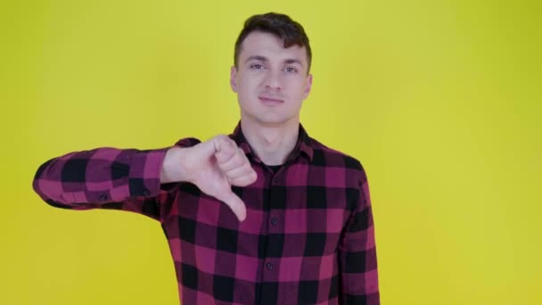 Man in een roze geruite shirt heft de hand en toont afkeer op een gele achtergrond - Video
