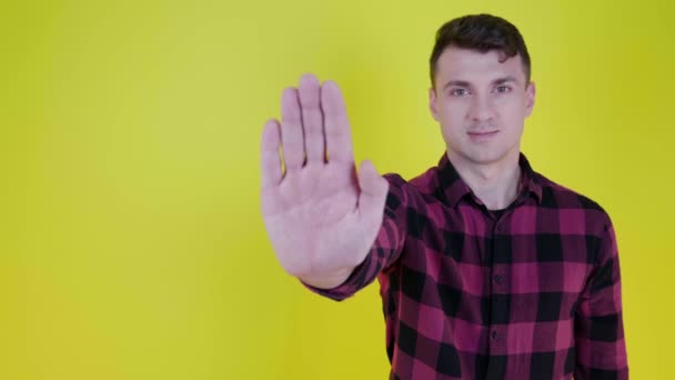 Ο άνθρωπος σηκώνει το χέρι, δείχνει παλάμη στην κάμερα και λέει να σταματήσει σε ένα κίτρινο φόντο - Πλάνα, βίντεο