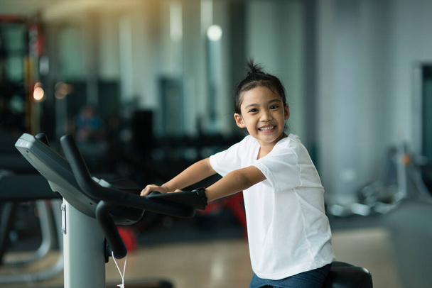 Маленька дівчинка використовує тренажерний велосипед у спортзалі. Фітнес-жінка використовує повітряний велосипед у спортзалі
. - Фото, зображення