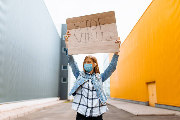 Młoda kobieta w medycznej masce ochronnej trzyma tekturowy plakietkę ze słowami Zatrzymać wirusa, na ulicy w mieście. Kwarantanna, koronawirus - Zdjęcie, obraz