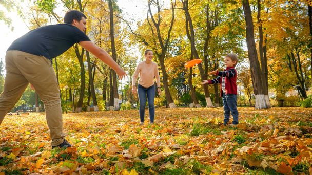 Szczęśliwa uśmiechnięta rodzina bawiąca się frisbee w jesiennym parku - Zdjęcie, obraz
