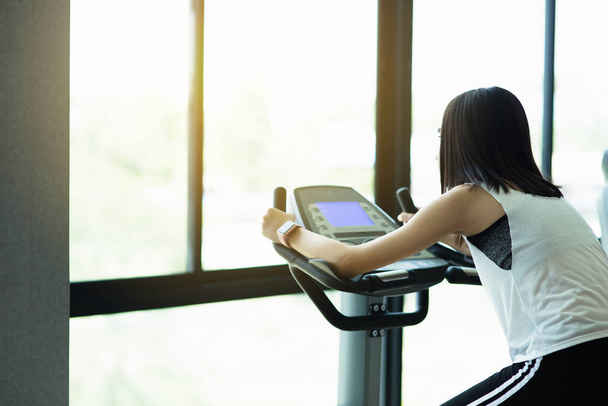 Fit young girl using exercise bike at the gym. Fitness female using air bike at gym. - Photo, Image