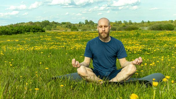Un homme chauve avec une barbe fait du yoga dans la nature
 - Photo, image