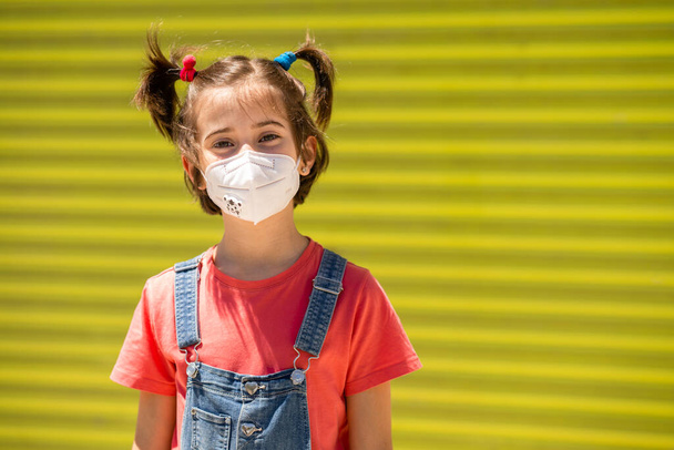 Child girl wearing a protection mask against coronavirus during Covid-19 pandemic - Photo, Image