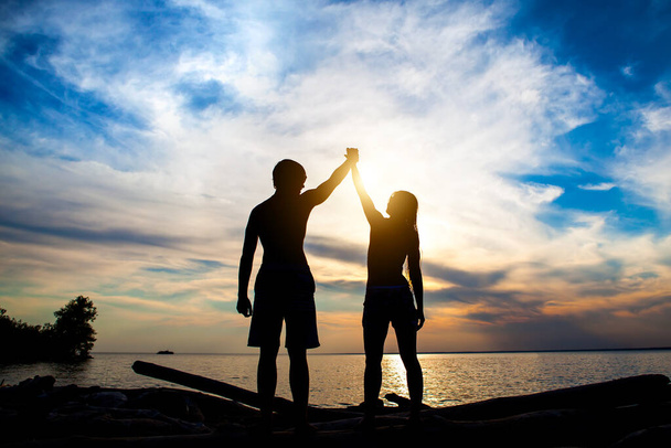 Happy pár silueta s rukama nahoru na pozadí západu slunce - Fotografie, Obrázek