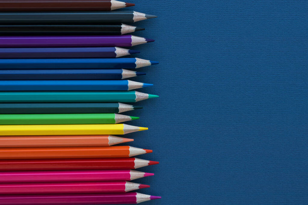 Koyu mavi arka planda çok renkli kalemlerin olduğu dikey bir sıra. Okula dönmek ve okul malzemeleri almak. Eğitici kavram. - Fotoğraf, Görsel