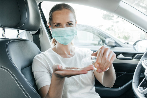 Young attracrive blonde girl wearing preventive mask smiling and cleaning her hands with hand sanitizer. Positive attitude during pandemic. New life. - 写真・画像