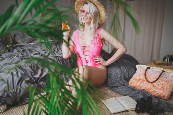 Mujer rubia sexy feliz en traje de baño rosa que imita el tiempo de vacaciones de verano en el interior del dormitorio de la casa. Situación del Coronavirus en la industria turística. Cuarentena divertida. Quédate en casa, Aislamiento
. - Foto, Imagen