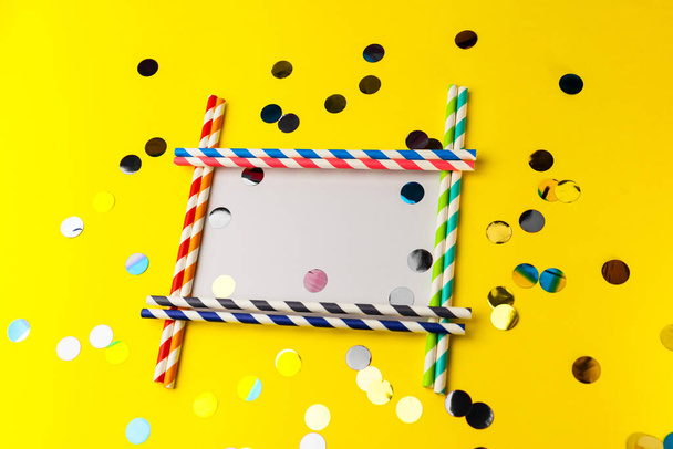 Empty frame from Multi-colored biodegradable paper tubes with place for your text. The concept of party, celebration, birthday. Copy space on Yellow Background with multicolored foil confetti. - Foto, Imagen