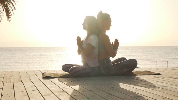 Due donne praticano la meditazione di chiusura per lo yoga di coppia al mare al tramonto
 - Foto, immagini