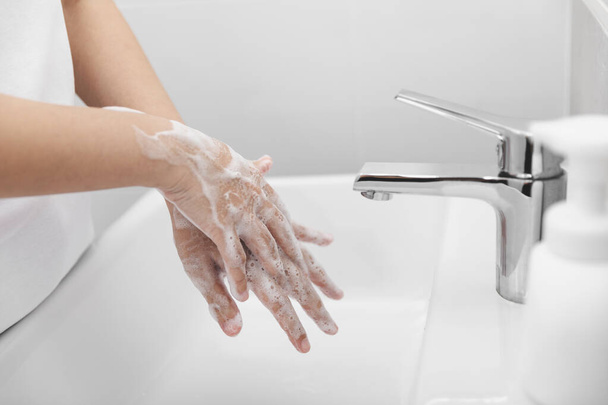 Nainen käyttää saippuaa ja pese kädet veden alla hanan koronaviruksen ehkäisyyn, hygieniaan sepelvaltimoviruksen leviämisen lopettamiseksi
. - Valokuva, kuva