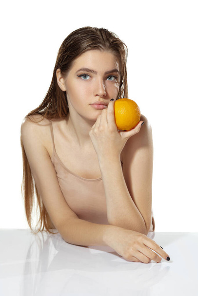 Healthcare. Beautiful young woman with orange over white background. Cosmetics and makeup, natural and eco treatment, skin care. - Fotografie, Obrázek
