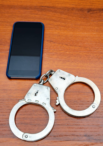 Handcuffs and Mobile Phone on the Wooden Table closeup - Foto, Imagem