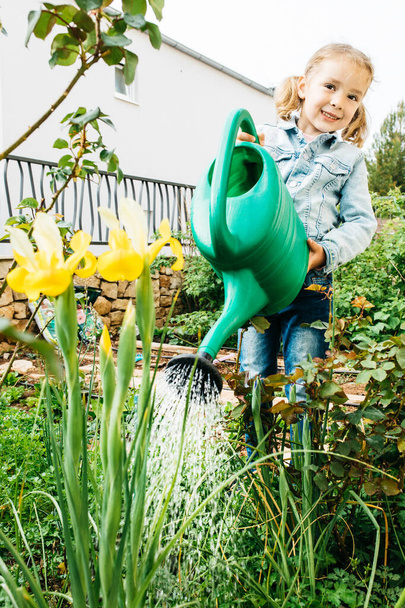 Életmód a kislány öntözés sárga virágok öntözőkanna a kertben tavasszal. Egy kis segítség. Egy kis kertész koncepció. Lassú élet. Önfenntartó koncepció. Kertészeti koncepció. - Fotó, kép