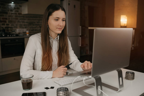 Fernstudium. Eine kaukasische Frau mit Kopfhörern, die auf ihrem Laptop ferngesteuert online lernt. Ein Mädchen beobachtet ein Webinar an ihrem gemütlichen Arbeitsplatz zu Hause. - Foto, Bild