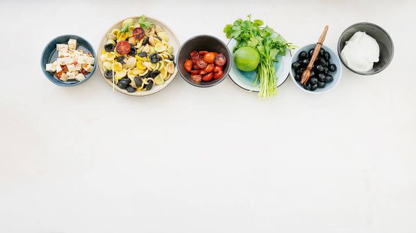 Makarna Salatası için eklentiler sıraya dizildi. Geleneksel İtalyan salatası. Orecchiette Arlecchino, kızarmış domates, soğan, siyah zeytin, limon, peynir, zeytinyağı, baharat ve otlar. Üst görünüm.  - Fotoğraf, Görsel