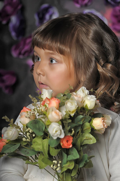 little brunette girl with curls with a white sweater with flowers in her hands on a floral background in the studio - Photo, image