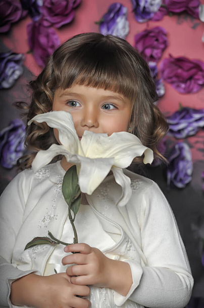 little brunette girl with curls with a white sweater with flowers in her hands on a floral background in the studio - 写真・画像