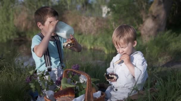 przekąski, głodne dzieci dobrze się bawią jedząc pieczenie i pijąc mleko ze szklanego słoika - Materiał filmowy, wideo