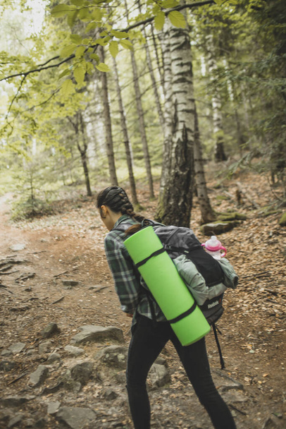 cool and stylish girl traveler with a backpack for a trip goes on a tourist route in the woods that leads to the top of the mountain - Foto, Imagem