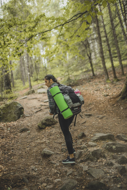 cool and stylish girl traveler with a backpack for a trip goes on a tourist route in the woods that leads to the top of the mountain - Фото, зображення
