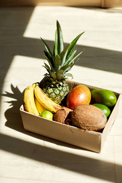 Organikus egzotikus gyümölcsök választéka dobozban, napfény. Zacskó egzotikus gyümölcsökkel a bejárati ajtóban, érintésmentes szállítás. Szolgáltatás-karantén pandémiás coronavirus. - Fotó, kép