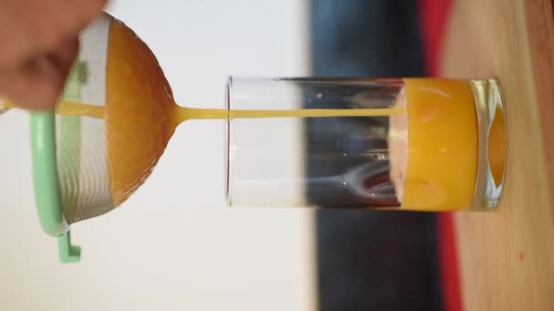 Mann gießt Orangensaft in der Küche seines Hauses in einen Glasbecher. Nährstoffreicher und energiereicher frischer Orangensaft. Videoaufnahmen mit Vertikal - Filmmaterial, Video