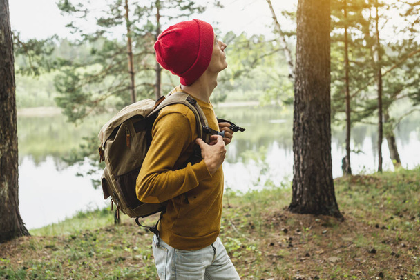 Een toerist met een rugzak en een rode hoed loopt in het bos tussen de bomen. Het concept van actieve trekking en eenheid met de natuur - Foto, afbeelding