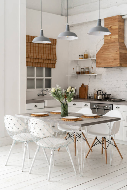 Vertikales Foto der weißen zeitgenössischen Küche mit modernem Interieur-Stil, Möbel, Esstisch, Gasherd, Backofen, Holzschränke, Arbeitsplatte und Spüle neben dem Fenster - Foto, Bild