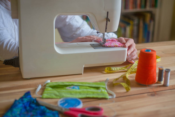 Nahaufnahme einer Frauenhände an einer Nähmaschine, die selbstgemachte Gesichtsmasken herstellt - Foto, Bild