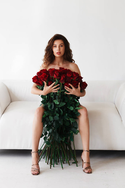 Bruna su un divano bianco con un grande mazzo di rose rosse
 - Foto, immagini