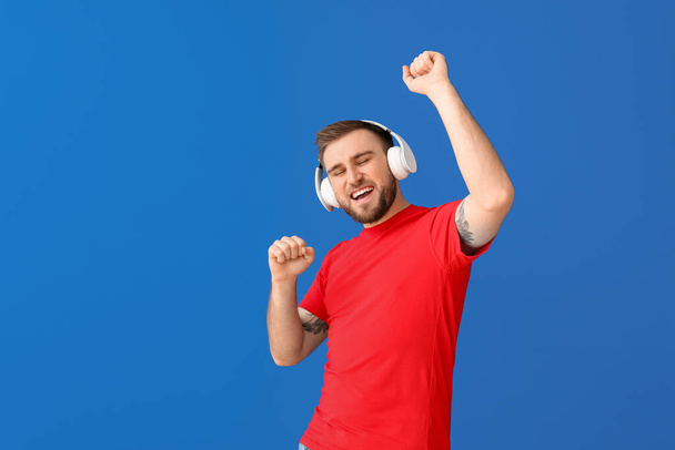 Handsome young man listening to music and dancing against color background - Fotoğraf, Görsel