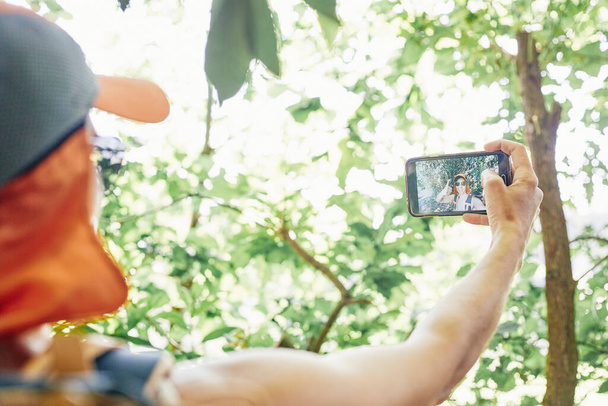 Frau macht beim Wandern ein Selfie in der Natur mit orangefarbener Tasse und Sonnenbrille - Foto, Bild