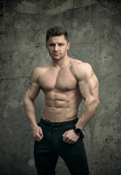 Hombre musculoso guapo posando sobre fondo de pared de hormigón. El concepto de fitness, culturismo, salud, estilo de vida. Retrato del modelo fitness
. - Foto, imagen