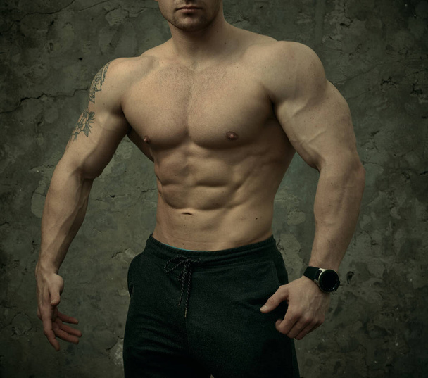 Hombre musculoso guapo posando sobre fondo de pared de hormigón. El concepto de fitness, culturismo, salud, estilo de vida. Retrato del modelo fitness
. - Foto, imagen