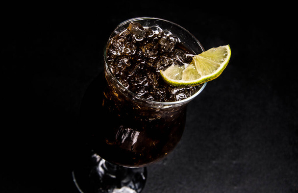 whiskey and coke cocktail. a glass with a drink on a black, isolated background. close-up of a slice of lime and ice. - Fotografie, Obrázek